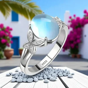 Anillo de plata con diseño floral y piedra central brillante sobre fondo mediterráneo.