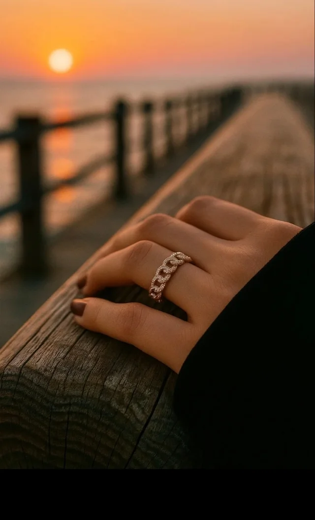Anillo tipo cadena chapado en oro 18K con circonitas, fotografiado al atardecer sobre una barandilla.